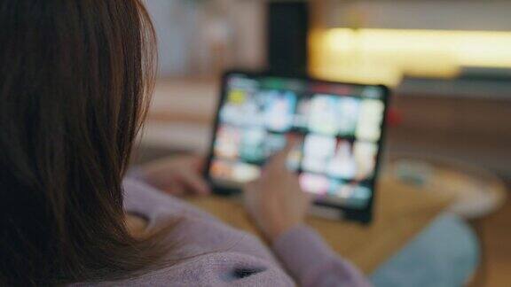 女性在家里客厅的沙发上休息时在平板电脑上选择互联网流媒体服务上的电影智能电视点播服务娱乐