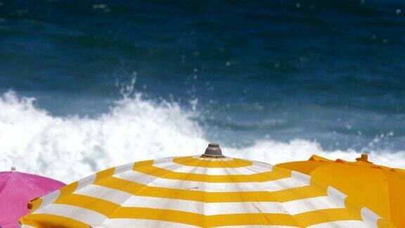 沙滩上撑着五颜六色的遮阳伞看着汹涌的海浪