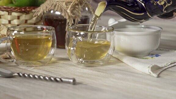 将热茶甘菊冲剂倒入白色朴素桌子上的两个杯子中