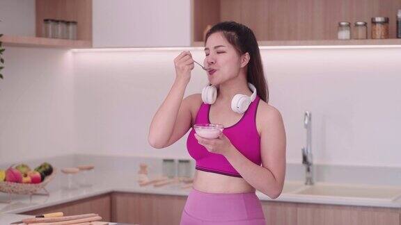 运动微笑的年轻亚洲女人穿着运动服吃健康的早餐在家里的厨房里吃酸奶
