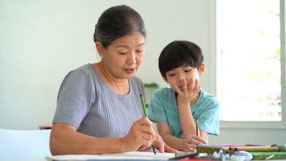 年长的亚洲妇女在家里教她的孙子中国传统书法