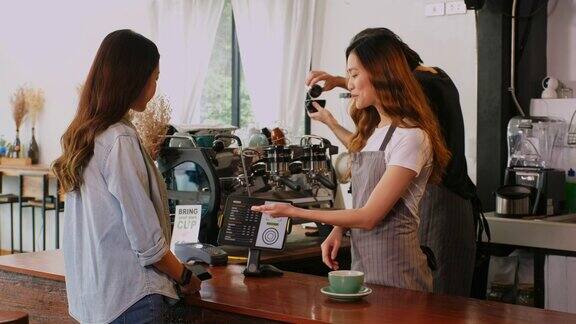 年轻的亚洲咖啡师在咖啡馆的柜台向亚洲女性顾客展示数字平板触摸屏上的咖啡菜单