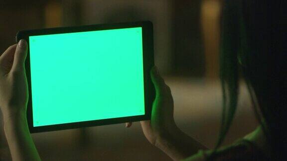 黑头发少女拿着平板电脑与绿色屏幕在风景模式在晚上时间休闲的生活方式