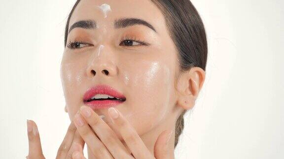 亚洲女性在白色背景上涂抹护肤霜美丽的女人用幸福的情感抚摸着自己的脸富有表现力的面部表情美容和温泉美丽的脸视频:多样化的肖像