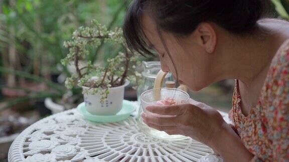 日常生活的可持续性亚洲成熟女性用有机茶玫瑰制作下午茶并在花园里休息为良好的状态竖起大拇指