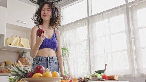 一名亚洲少女戴着耳机听着音乐用水果刀和朋友们在厨房里做蔬菜沙拉快乐地生活在一起烹饪娱乐生活中很少奢侈