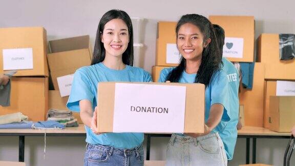 描绘年轻的亚洲妇女和年轻的黑人妇女微笑着拿着小捐赠盒看着相机肖像友谊团队成功志愿慈善领导人慈善理念