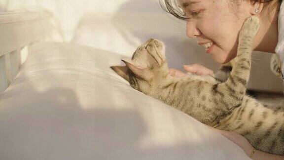 一个女人在卧室白色的床上拥抱和亲吻她的宠物小猫的肖像
