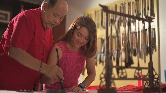 一位亚洲华人父亲在练习中国新年的书法并在一张红纸上教他的女儿握着她的手