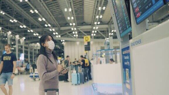 一名亚洲女子戴着医用口罩在国际机场用智能手机查询航班