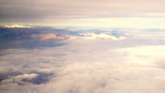 云和雪覆盖的阿尔卑斯山脉的鸟瞰图透过一架喷气式飞机的窗户在日落时分大陆飞行