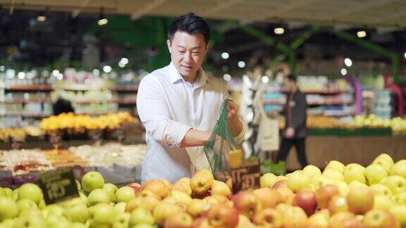 年轻的亚洲人在超市里挑选环保袋装的苹果水果或蔬菜站在杂货店柜台附近的男性顾客买东西扔东西