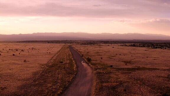 新墨西哥沙漠公路的乡村景象:夕阳下汽车行驶在一条土路上