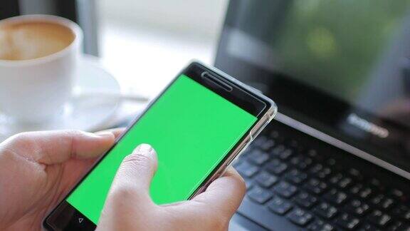 女人用手触摸绿色屏幕的智能手机用笔记本电脑拍摄
