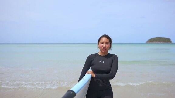 亚洲女人在莽撞的警卫手持冲浪板在海滩上行走