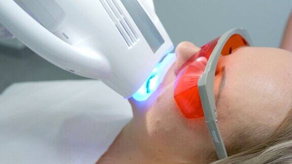 BeyondPolusePlus高级美白系统与牙科紫外线激光美白设备医生正在等待完成牙齿美白手术的女患者的橙色护目镜