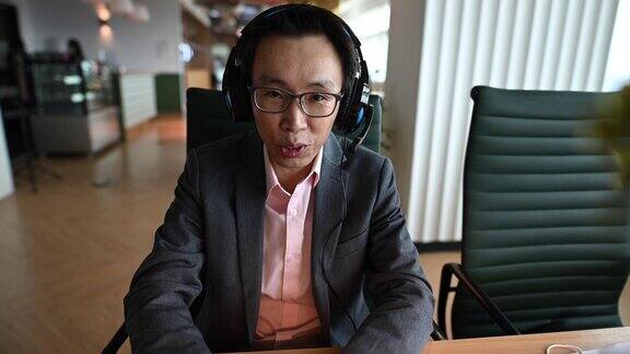 一名亚裔华人中年白领戴着口罩对着摄像机进行视频通话与他的商业伙伴进行视频会议
