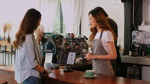 年轻的亚洲咖啡师在咖啡馆的柜台向亚洲女性顾客展示数字平板触摸屏上的咖啡菜单