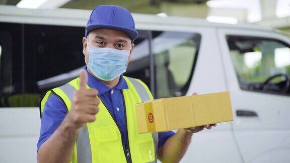 快邮配送服务理念年轻的亚洲快递员戴着防毒面具站在白色汽车前一手拿着包裹大拇指对着相机4k决议