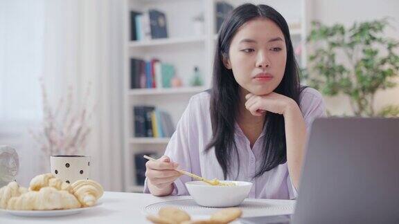 亚洲女性吃面条在笔记本电脑上看电视剧不健康的饮食习惯