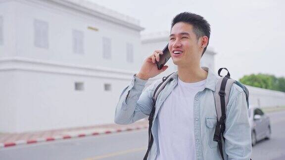 亚洲有吸引力的年轻男子背包客讲电话走在城市英俊的男性游客独自在街上旅行使用智能手机享受在泰国度假旅行的时间