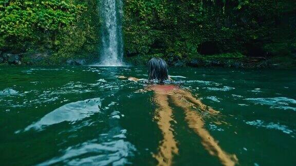 年轻女子游泳到瀑布