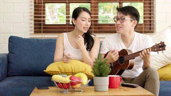 年轻的亚洲结婚幸福的夫妇在玩尤克里里和唱歌在客厅幸福的夫妇放松周末一起在家里