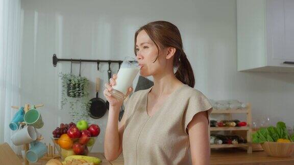 亚洲年轻美丽的女孩喝一杯牛奶在家里的厨房有吸引力的口渴的女人持有和啜饮一杯牛奶后早上醒来在家里的健康保健福祉
