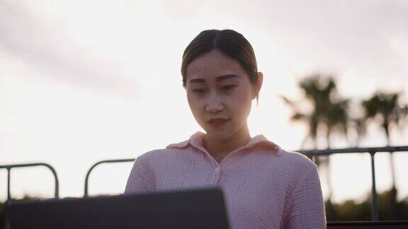 年轻的亚裔女大学生在公园户外使用笔记本电脑进行在线学习