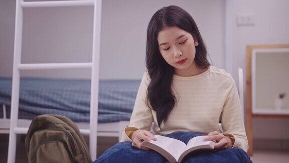 一名年轻的亚洲学生穿着休闲服坐在宿舍的双层床上全神贯注地看书在舒适的宿舍里她靠在双层床凸起的靠背上休息