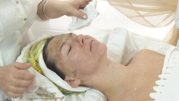 美容师在美容院用餐巾擦拭女性脸上的绿泥面膜
