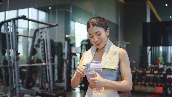 疲惫的亚洲妇女的肖像在运动服饮用瓶装水在健身房女运动员补充水平衡后健身锻炼练习或训练后口渴