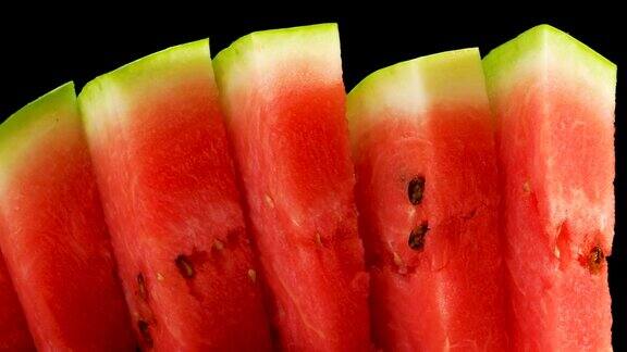 成熟多汁的天然西瓜切成薄片的红色西瓜在黑色的背景上旋转
