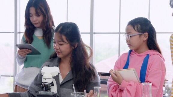 在小学科学课上小女孩尝试用显微镜观察放在桌子上的微生物她在做实验笔记