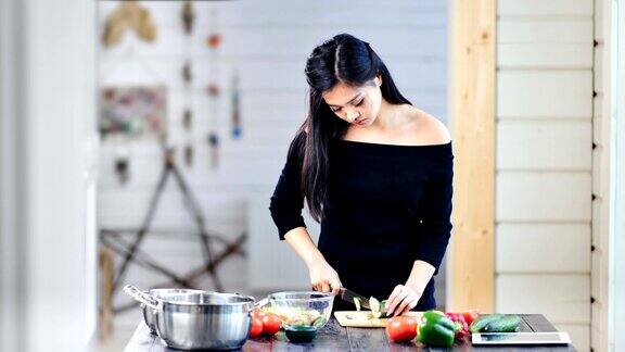 自信的年轻亚洲女性烹饪健康新鲜的沙拉用刀切有机蔬菜