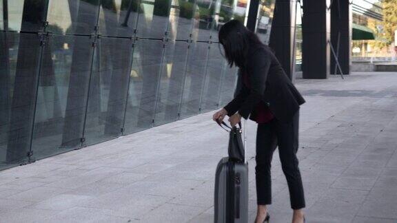 一位女商人从手提包里拿出手机手提包放在行李箱上