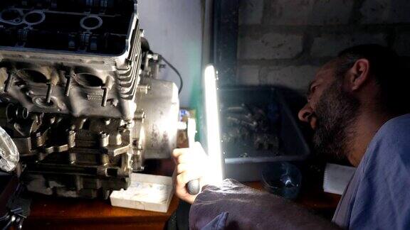 细心的机械师在车库或车间修理汽车发动机在黑暗中用明亮的手电筒工作的人修理工正在维修汽车慢动作特写侧视图