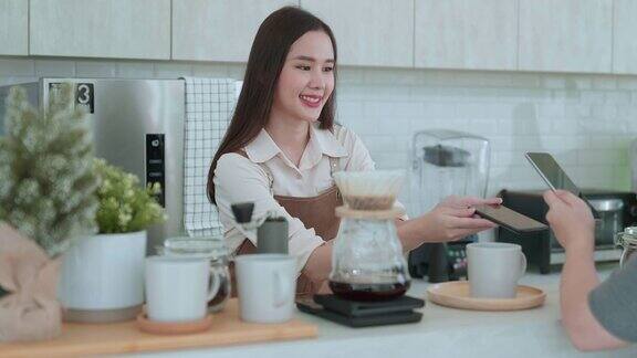 微笑的咖啡师为她的顾客提供咖啡亚洲妇女在咖啡店用智能手机支付二维码咖啡