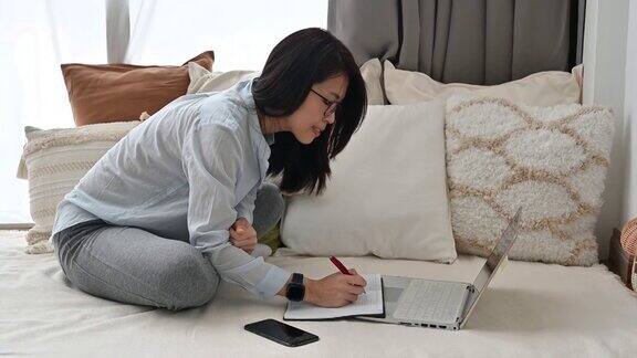 一个亚洲女性坐在沙发上用笔记本电脑和笔记在客厅工作