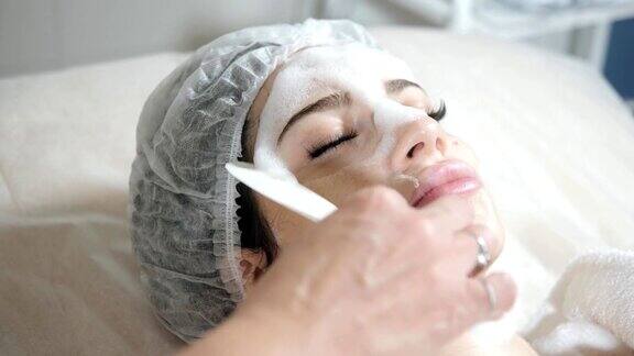 用抹刀去除脸上的泡沫年轻漂亮的女人正在美容院接受治疗洁面泡沫使用