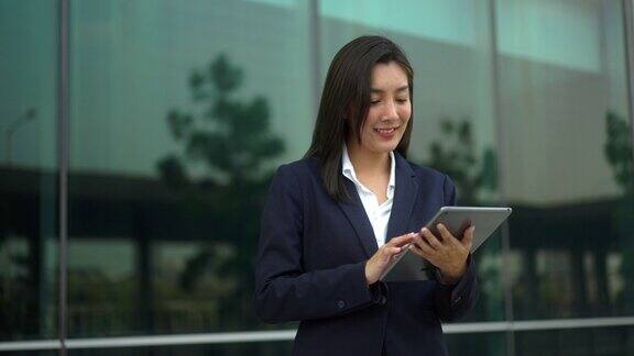 商务人士步行和使用平板电脑应用程序与技术交流在城市的商业大楼成功女性在现代办公大楼前使用手机工作的女人