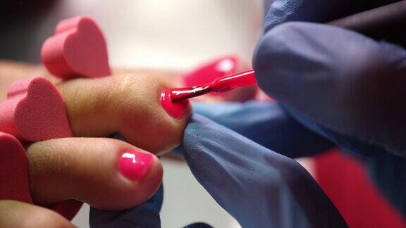 美甲师在女性指甲上涂上粉红色的指甲油用刷子戴着手套
