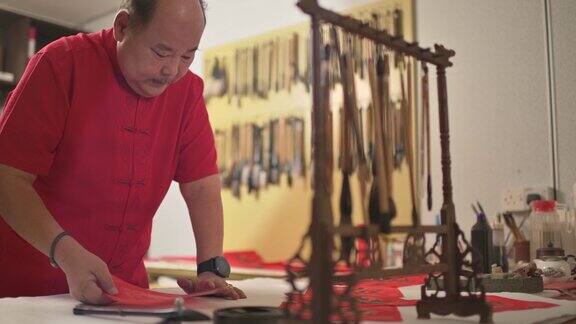 亚洲华人男性练习书法为即将到来的中国新年庆祝家庭装饰目的与繁荣和良好的措辞写在一张红色的纸上