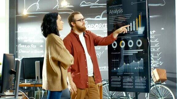 女性开发人员和男性统计人员使用交互式白板演示触摸屏查看图表、图表和增长统计数据他们在时尚创意办公室工作