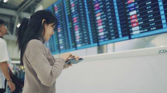 一名亚洲女子在机场用智能手机和手表查看登机牌时刻表