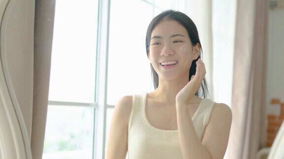 慢动作肖像年轻的亚洲妇女使用面霜在她的脸上概念为新鲜滋润肌肤美丽近距离美容脸快乐健康模式年轻的黑发女孩照顾她的皮肤
