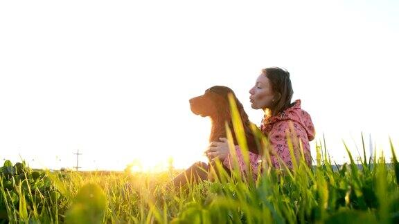 日落时分女人和狗玩耍小女孩和宠物坐在草地上在大自然中放松