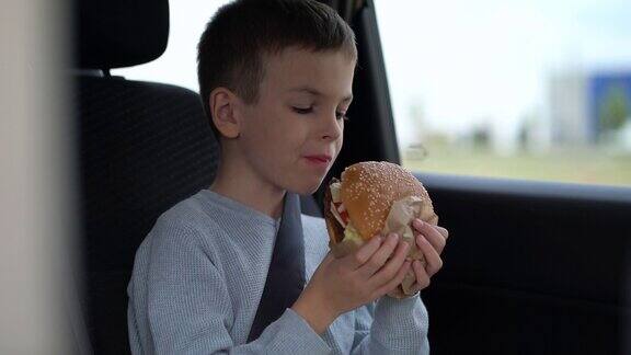 一个男孩在停车场的汽车后座上吃一个大汉堡一名学生正在享受快餐店提供的多汁汉堡