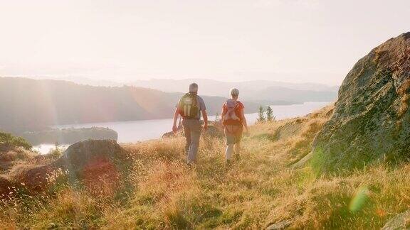 慢动作后视图拍摄的老年夫妇行走在山顶徒步通过美丽的乡村在湖区英国