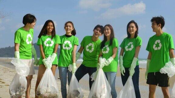 一群年轻的亚洲人志愿者穿着绿色t恤站在镜头前拿着清理海滩后收集的垃圾垃圾袋生态安全概念4k决议